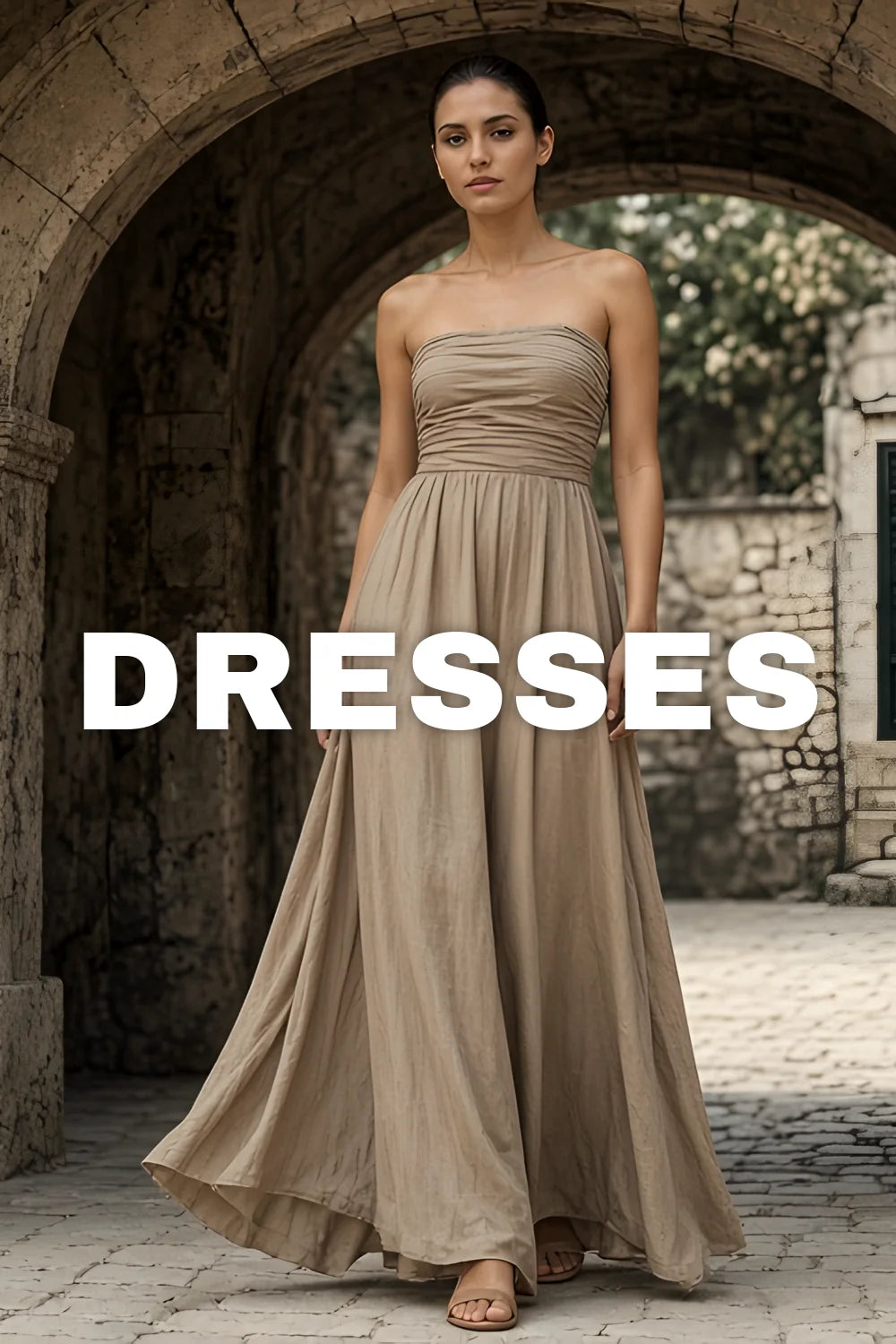 Dresses — woman in a taupe strapless pleated maxi dress under a stone archway